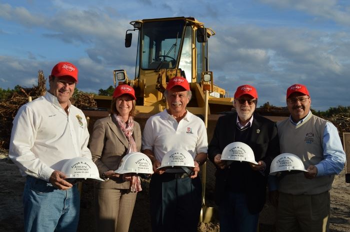 City Council Members wearing caps and holding hard hats in front of a tracto